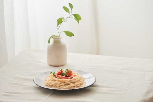 Food, spaghetti bolognese sauce in white dish and a vase of plants on a white prepared table