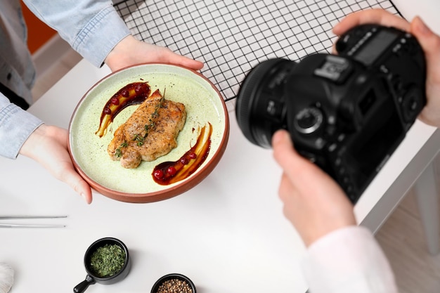 Photo food stylist holding plate with delicious meat medallion while photographer taking photo in studio closeup