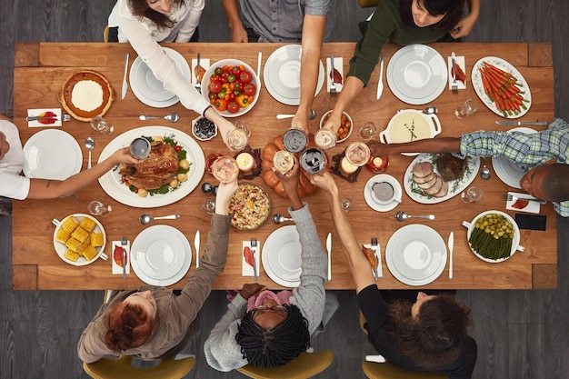 Food top view and friends toast at a table in celebration of thanksgiving at a party or social event together Cheers support and happy people with diversity support and trust enjoy a dinner meal