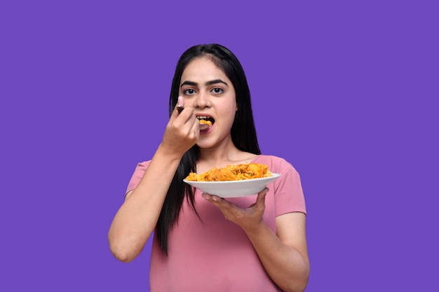 foodie girl eating biryani with spoon over purple background indian pakistani model