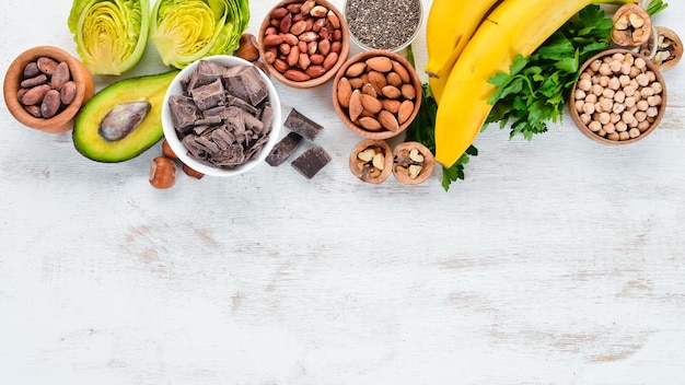 Foods containing natural magnesium Mg Chocolate banana cocoa nuts avocados broccoli almonds Top view On a white wooden background