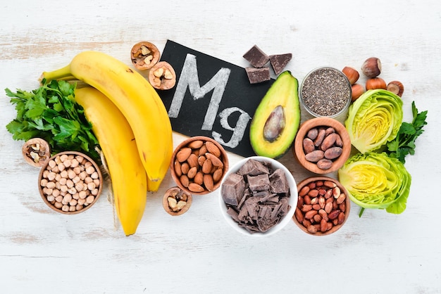 Foods containing natural magnesium Mg Chocolate banana cocoa nuts avocados broccoli almonds Top view On a white wooden background