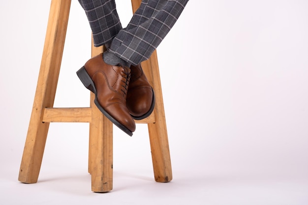 foot hanging from wooden stool with brown shoes with a white background