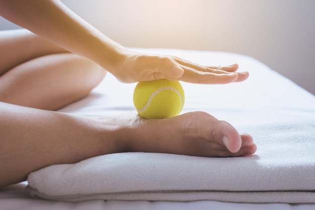 Foot soles massageWoman hands giving massage with tennis ball on foots in bedroom