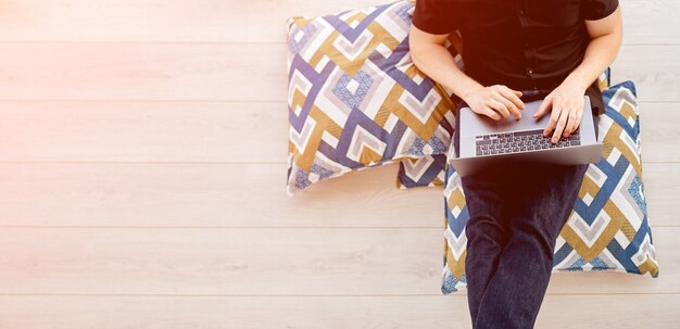 Footage from above as the man remotely works behind his laptop on his balcony, sitting on pillows, computer on his feet. High quality photo