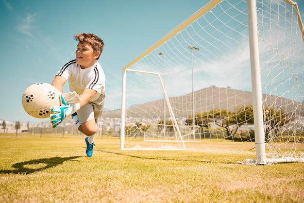 Football boy goalkeeper and jump saving ball from goals at outdoor sports field Soccer kid and competition game with fitness goal keeper and soccer ball on grass success and action to save goal