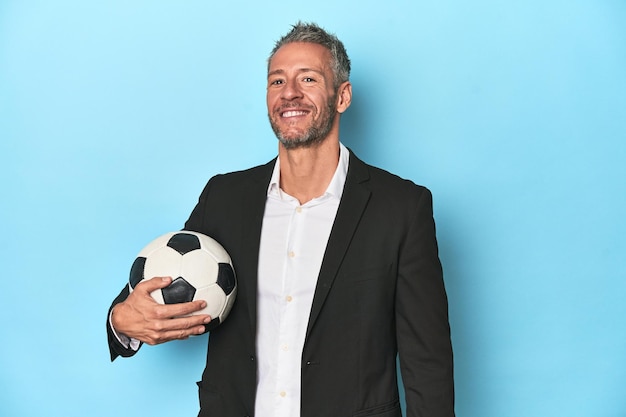 Football coach with soccer ball on blue studio backdrop