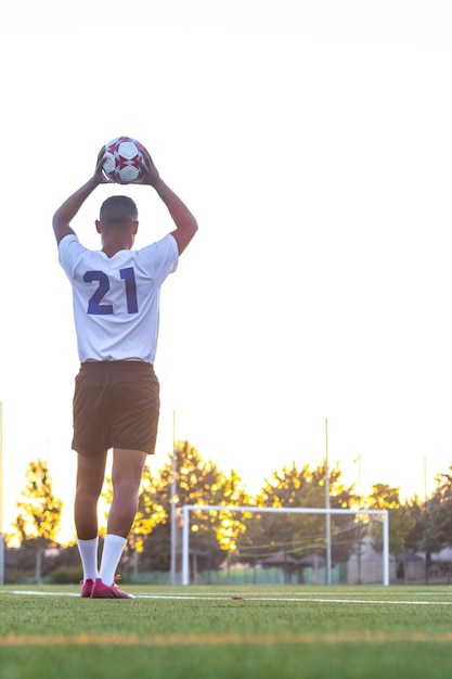 Football player raising the ball throwin Rear view of soccer player throwing the ball with his hands on the playing field Football player doing throwin