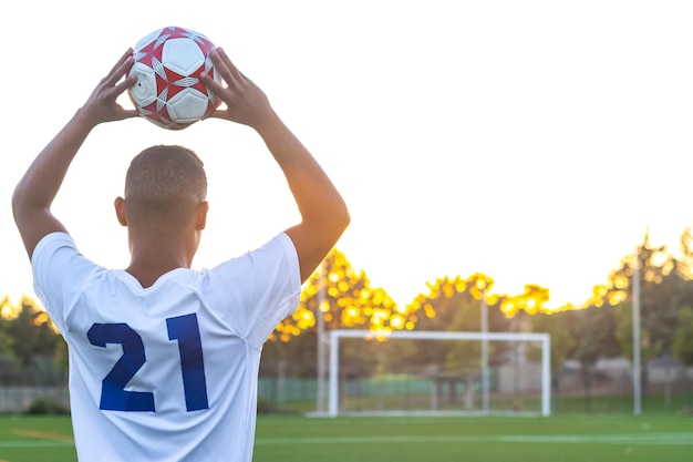 Football player raising the ball throwin Rear view of soccer player throwing the ball with his hands on the playing field Football player doing throwin