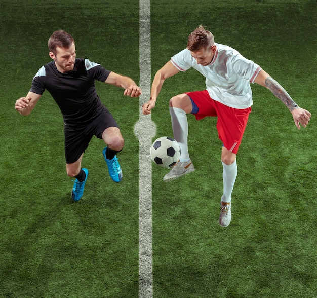 Football player tackling for ball over green grass background. Professional male soccer players in motion at stadium. Fit jumping men in action, jump, movement at game.