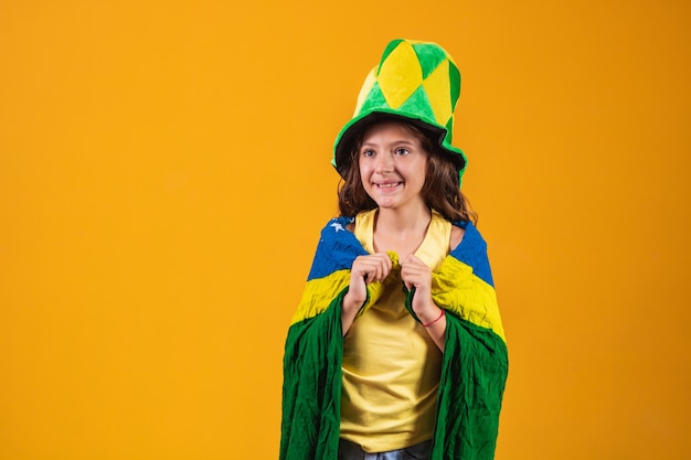 Football supporter, Brazil team. Beautiful little girl cheering for her team on yellow background