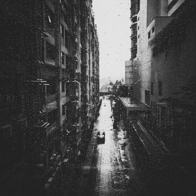 Footpath amidst buildings seen through seen wet window during rainy season