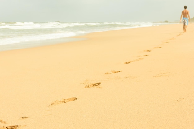 Footprints on empty beach with man on background in a cloudy morning in Bentota Sri Lanka