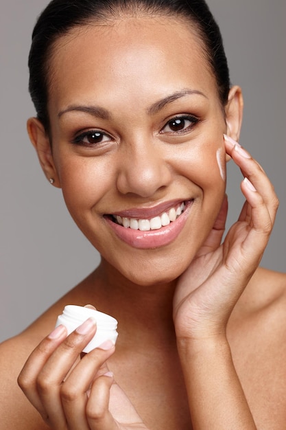 Forever young Cropped shot of a beautiful young woman applying face cream while standing in a studio