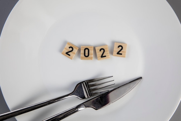 Fork and knife on a white empty plate with  text top view new year diet healthy eating concept backg