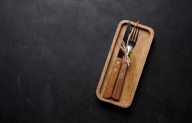 Fork and knife with wooden handle on black background top view