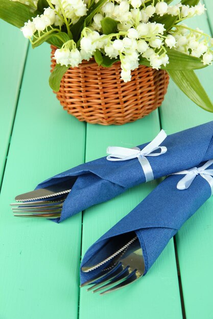 Fork and knife wrapped in blue paper napkin on color wooden background