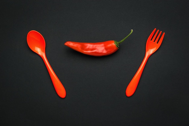 A fork a spoon and a pod of red pepper on a black background