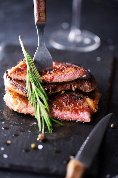 Fork in steak on black plate plate with rosemary and pepper, selective focus