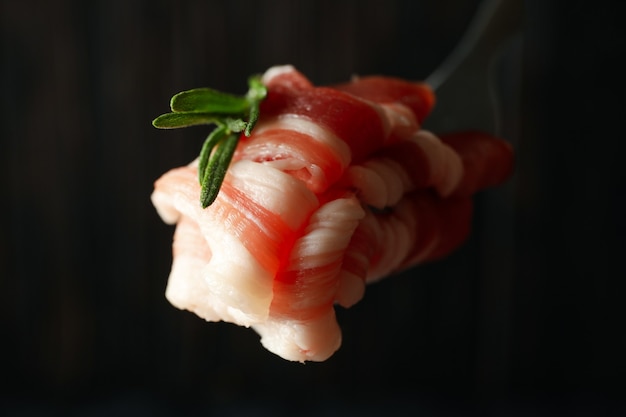 Fork with bacon on blurred wooden surface, close up