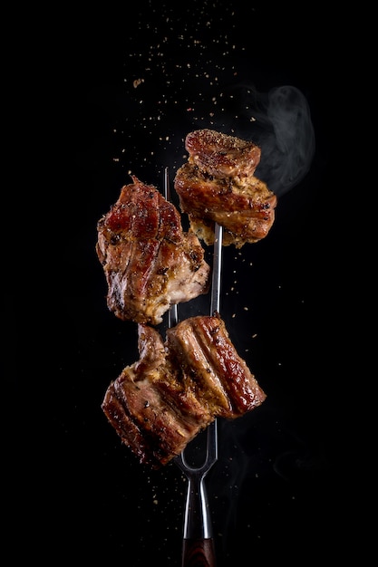 Fork with pieces of delicious barbecued meat on black