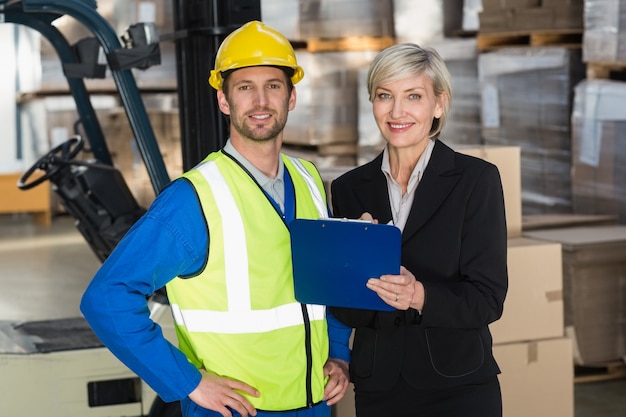 Forklift driver and his manager smiling at camera in a large warehouse