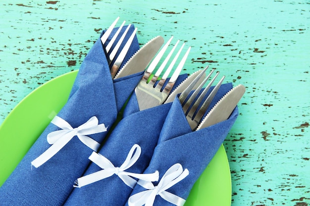 Forks and knives wrapped in blue paper napkins on color wooden background