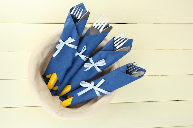 Forks and knives wrapped in blue paper napkins on color wooden background