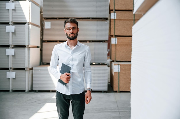 In formal clothes Storage worker is in the warehouse with bunch of products