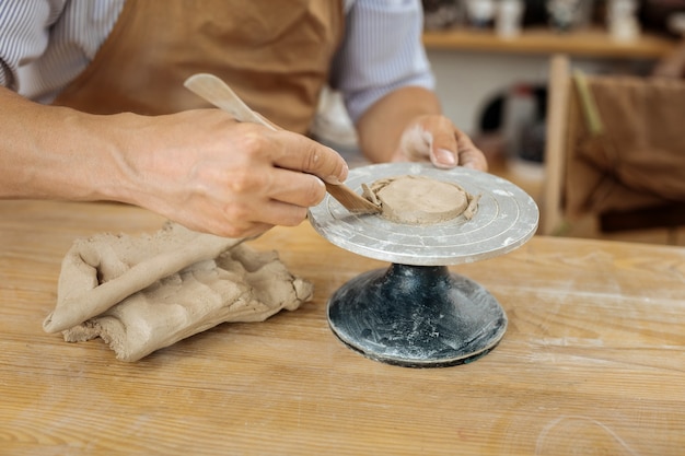 Forming clay items. Handicraftsman wearing dark brown apron forming future clay items in his workshop