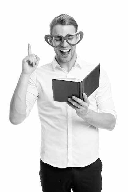 Found answer Man handsome young pointing upwards and laughing Man happy face in heart shaped eyeglasses reading book Guy found answer in book isolated white background Nice idea