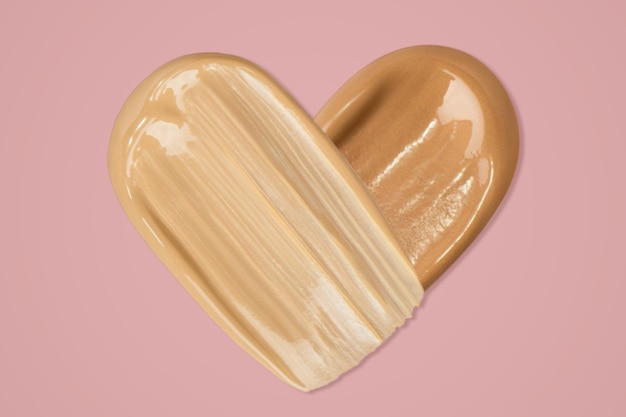 The foundation is smeared in the shape of a heart on a light pink background Tone cream