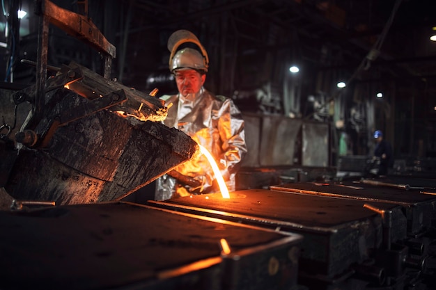 Foundry workman pouring molten iron into molds for steel production, heavy industry and metallurgy process.