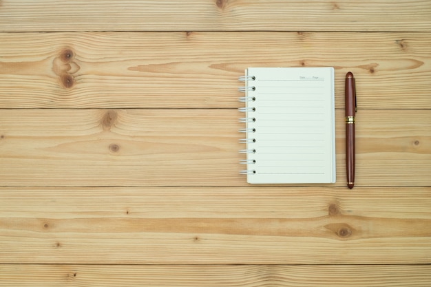 Fountain pen or ink pen with notebook paper on wood table