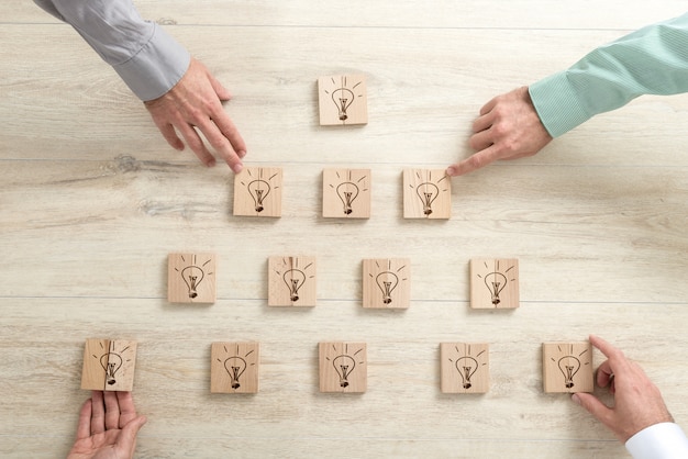 Four business people placing wooden blocks with light bulbs in a form of a pyramid