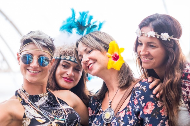 Four cheerful beautiful young women celebrate together and take a selfie picture smiling and having fun in friendship party concept with colored dress and flowers crowd bright background people happy