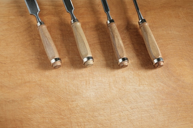 Four chisels with wooden handles of different sizes lie at the top of the wooden table, and copyspace remains below.