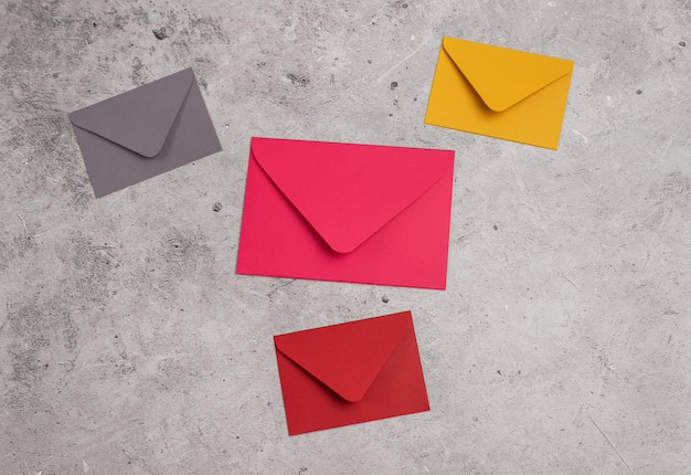 Four envelopes of a different color on a light concrete background