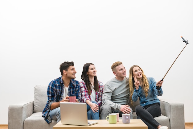 The four friends make a selfie on the sofa on the white wall background