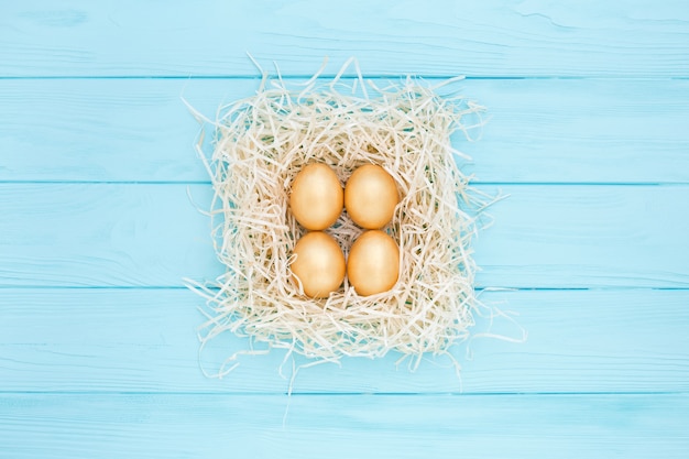 Photo four golden easter eggs in square nest on blue background, flat lay.