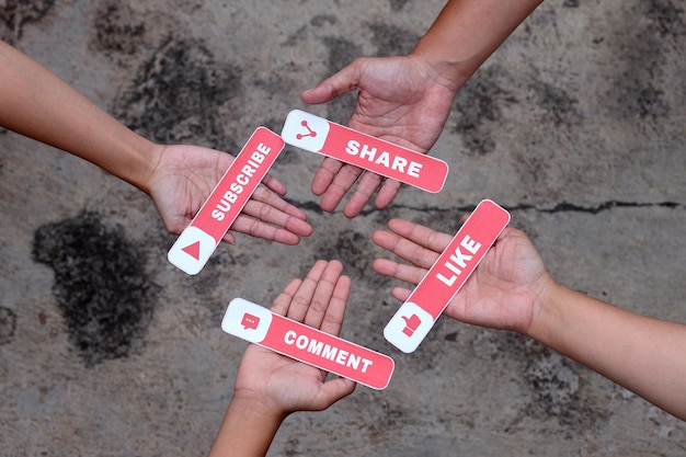 Four hands of young people holding printed paper with Like, Comment, Share, and Subscribe text. Vlog