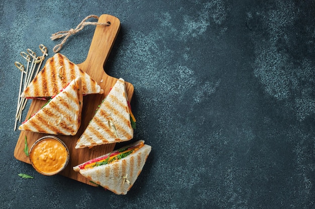 Four homemade sandwiches with sausage cheese and arugula on a dark concrete background