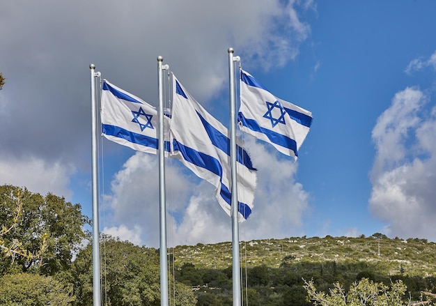 Four Israeli flags proudly waving under the blue sky with hills in the background