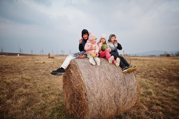 Four kids with fruits in hands sitting on haycock at field