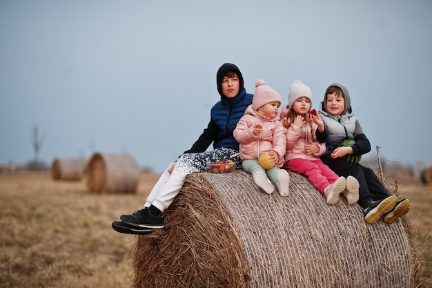 Four kids with fruits in hands sitting on haycock at field