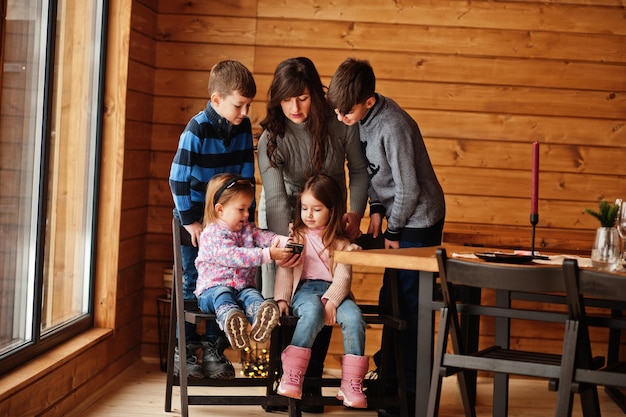 Four kids with mother in modern wooden house watching video in mobile phone