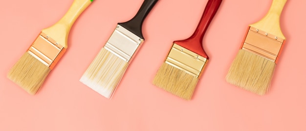 Four paint brushes lined up on a pink background.