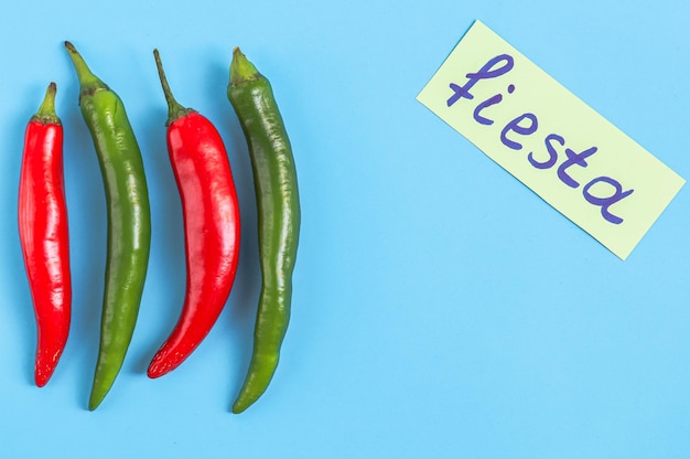 Four pieces of hot red and green chili peppers with yellow note fiesta on a light blue