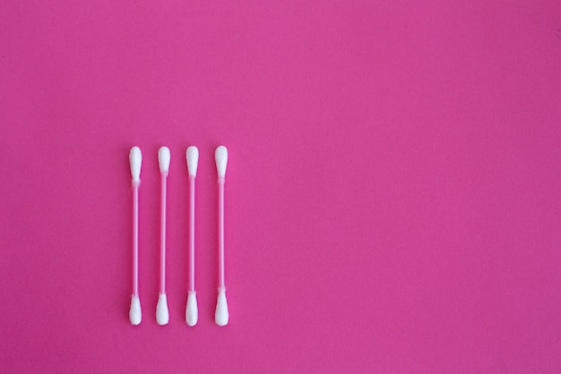 four pink cotton buds with white heads laid out in vertical line on a pink background