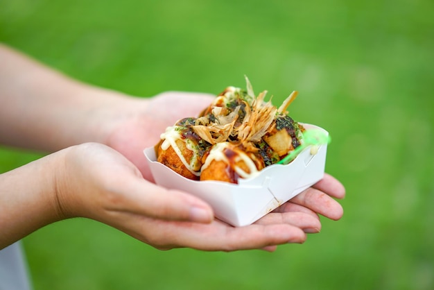 Four Takoyaki Local Japanese octopus meat ball in the hand with blur grean background ready to eat